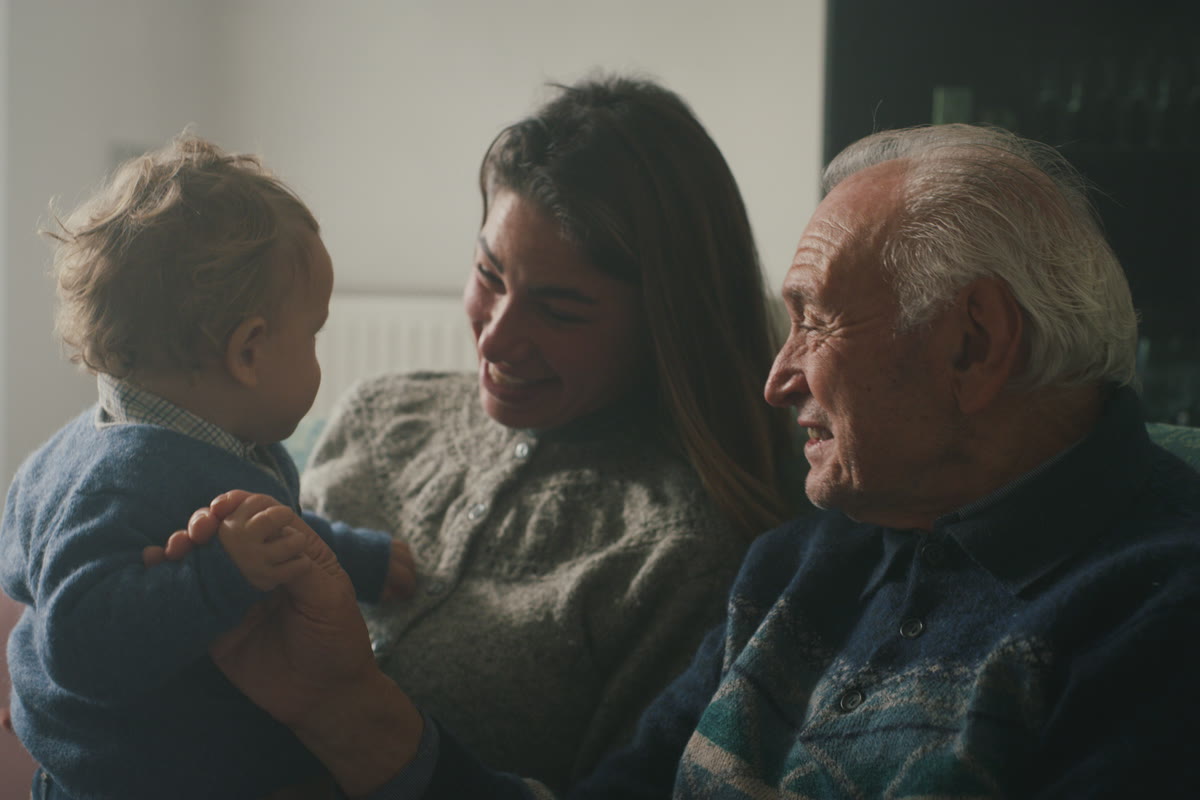 Un abuelo, su hija y el bebé de ella sentados juntos en un sofá en casa.