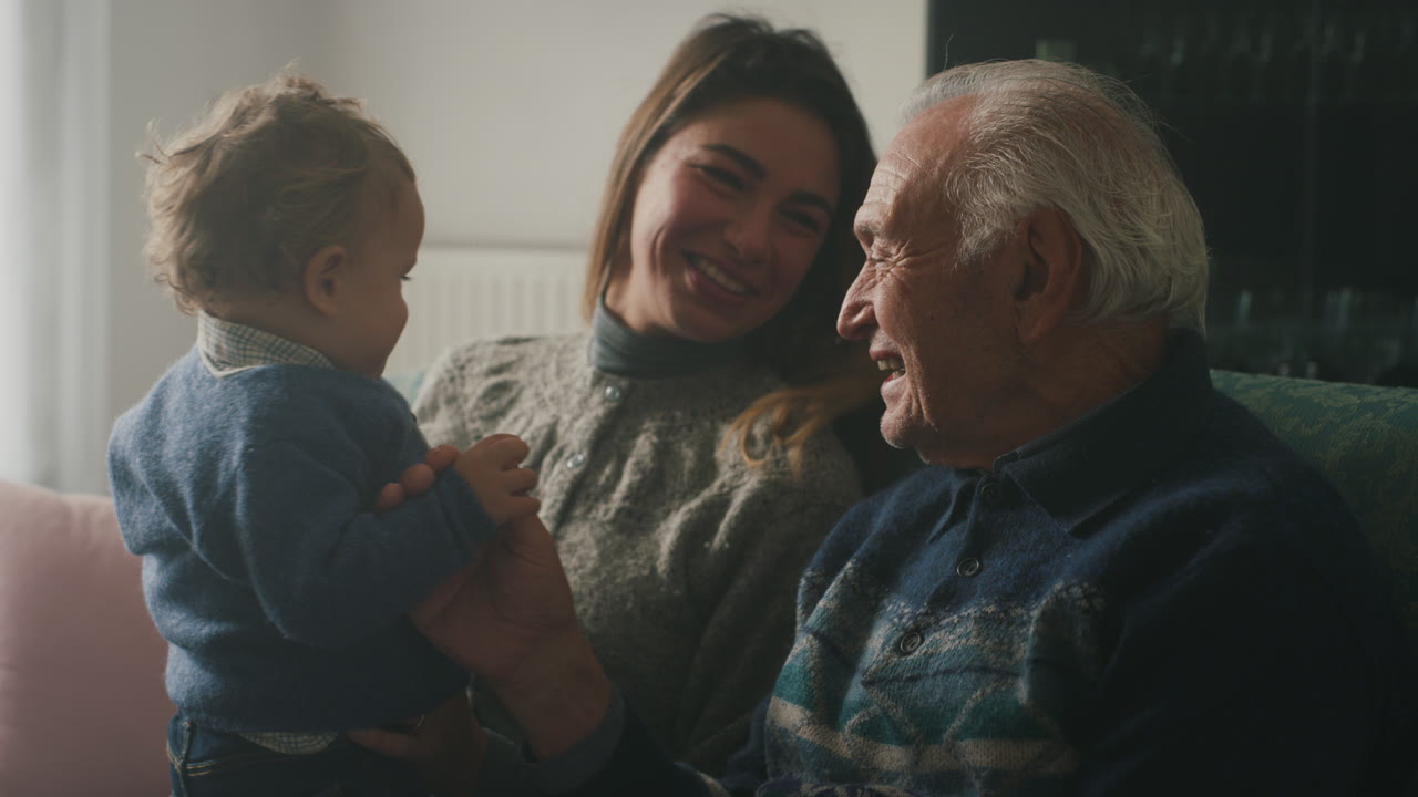 Un abuelo, su hija y el bebé de ella sentados juntos en un sofá en casa.
